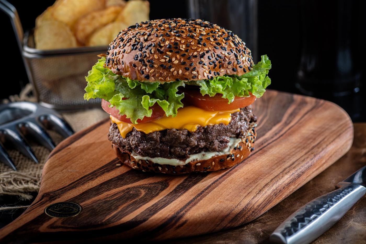 Burger garni de salade, tomate et cheddar sur une planche