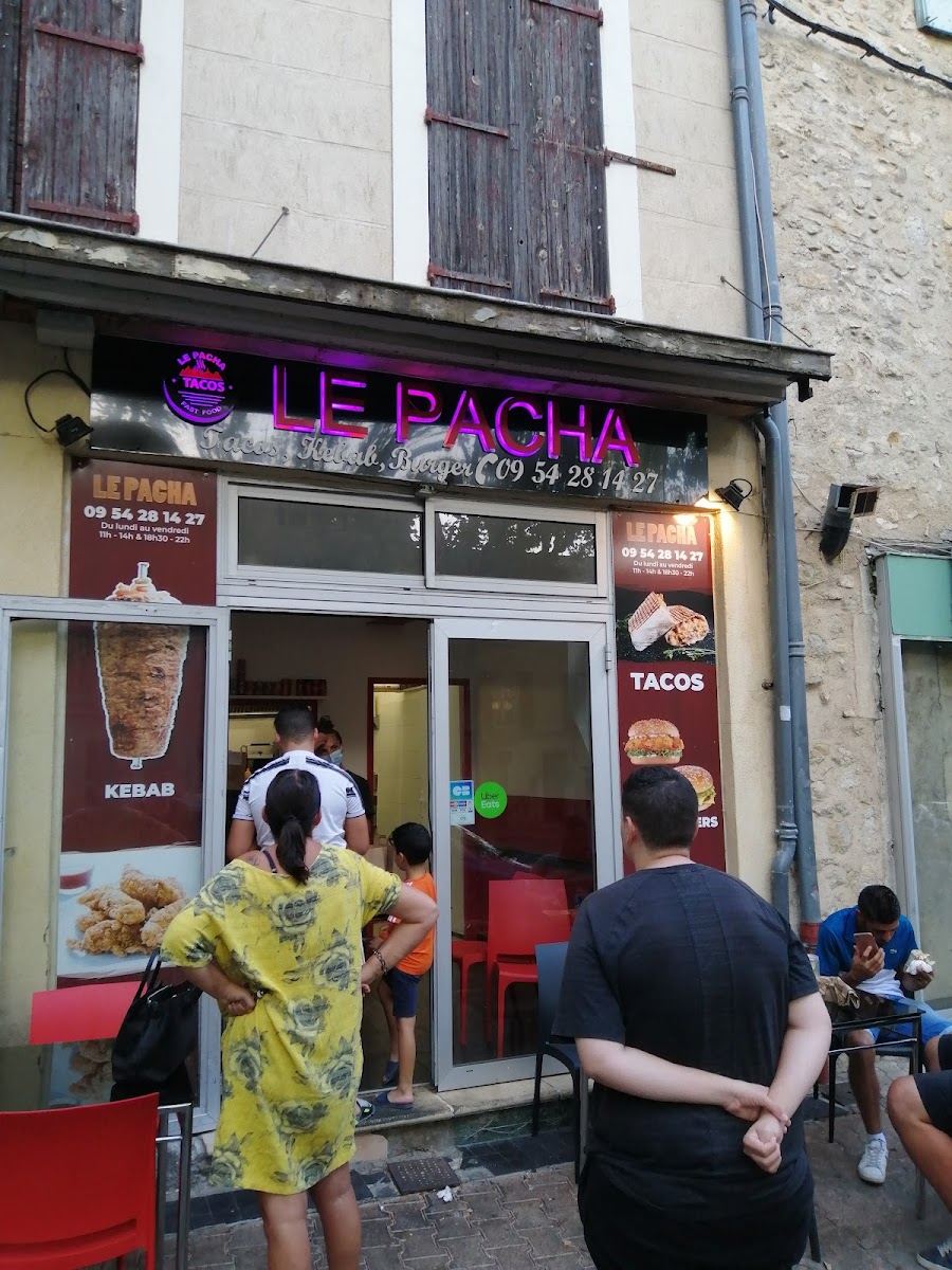Devanture du snack Le Pacha avec son enseigne néon et des clients qui patientent