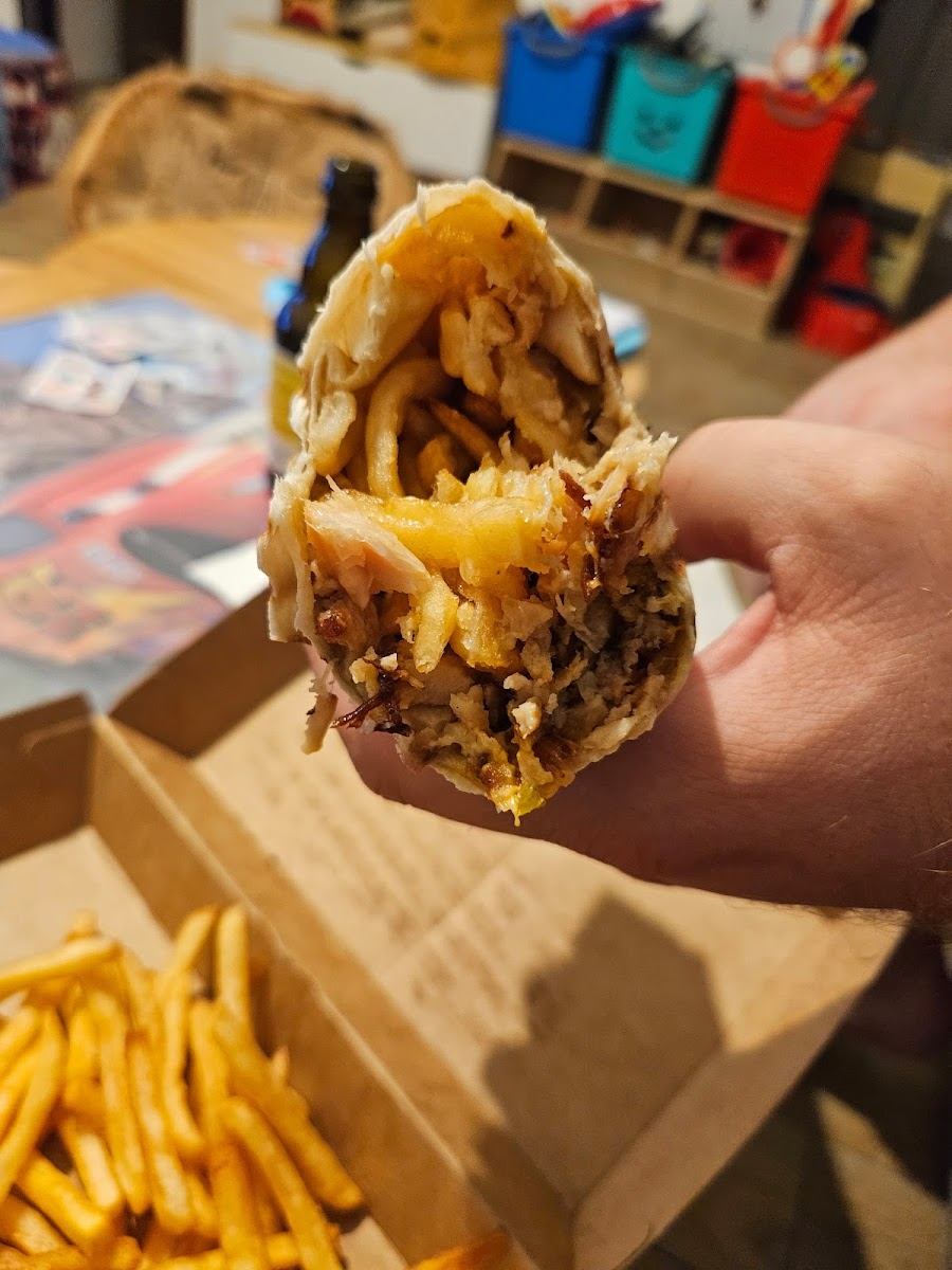 Kebab bien garni tenu à la main au-dessus d'une barquette de frites