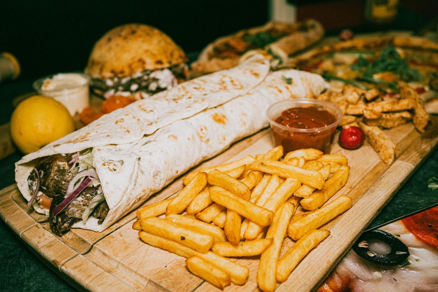 Kebab roulé dans sa galette posé sur une planche avec des frites et de la sauce