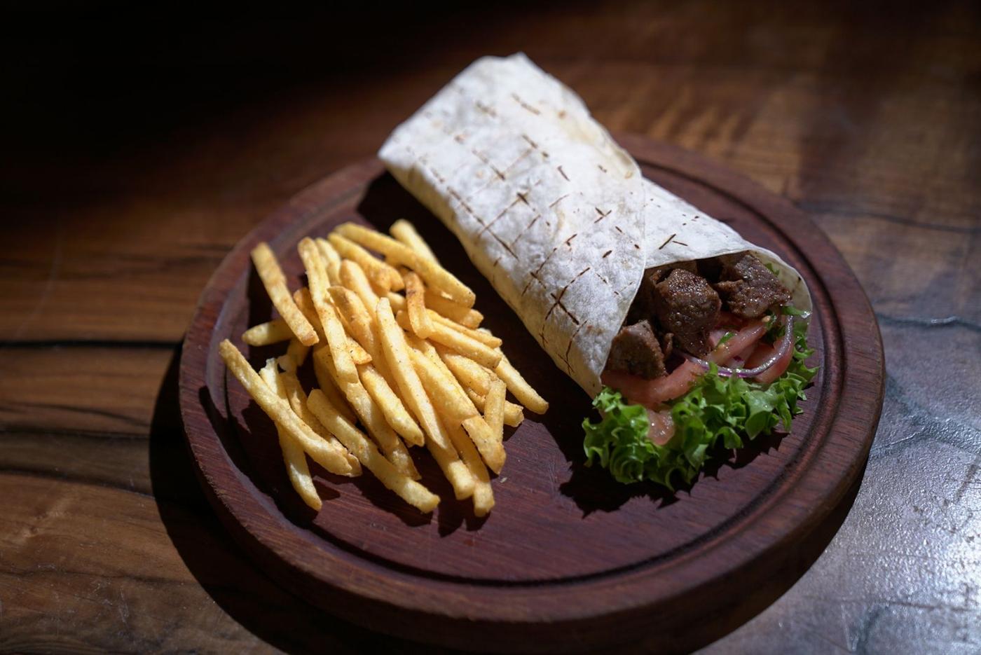 Tacos grillé posé sur une assiette en bois sombre, avec des frites